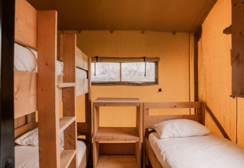 Interior de una tienda glamping con litera y cama individual en Holiday park Eigen Wijze, Países Bajos.