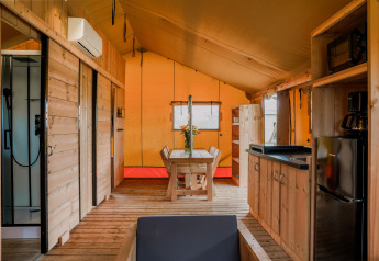 Interior de una tienda glamping safari en Holiday Park Eigen Wijze con muebles de madera y comodidades modernas.