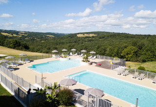 Vista de la zona de piscina con tumbonas y sombrillas en Camping Domaine de la Faurie, Occitania, Francia.