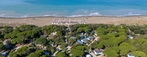 Aerial view of Sandaya Etruria holiday park in Tuscany, Italy, showing trees, cabins and sandy beach.