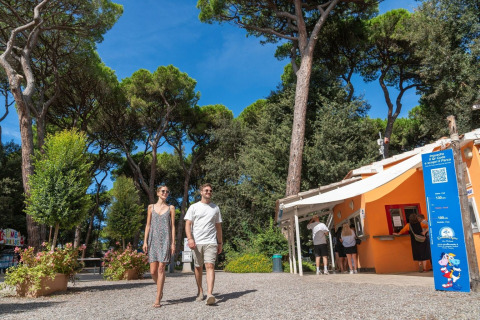 Koppel wandelt op zonnige dag bij Sandaya Etruria vakantiepark, omringd door bomen in Toscane, Italië.