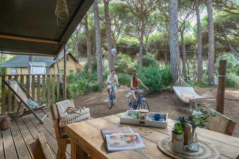 Twee mensen fietsen bij Sandaya Etruria vakantiedomein in Toscane, Italië, omringd door pijnbomen.