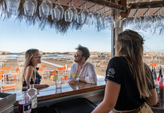 A couple enjoys drinks at the beachfront bar of Sandaya Etruria holiday park in Tuscany, Italy, served by staff.