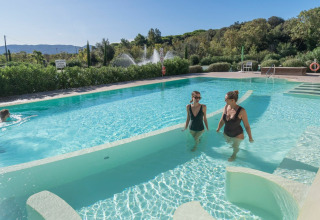 Twee dames genieten van het zwembad bij Sandaya Etruria vakantiepark in Toscane, Italië, met groene omgeving.