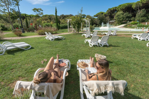 Due donne si rilassano su lettini al parco vacanze Sandaya Etruria in Toscana, Italia, in una giornata soleggiata.