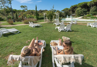 Two women relaxing on sun loungers at Sandaya Etruria holiday park in Tuscany, Italy, on a sunny day.