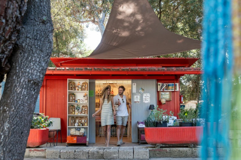Koppel wandelt uit rood winkeltje in Sandaya Etruria vakantiepark, tussen bomen in Toscane, Italië.
