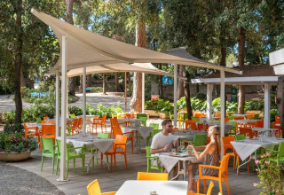 Udendørs restaurantområde med farverige stole og borde under sejlskygger i Sandaya Etruria, Toscana.