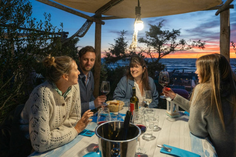 Quattro amici cenano all'aperto al tramonto al villaggio turistico Sandaya Etruria in Toscana, Italia.