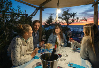 Quattro amici cenano all'aperto al tramonto al villaggio turistico Sandaya Etruria in Toscana, Italia.