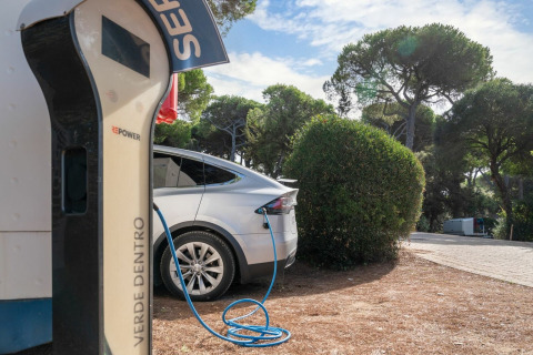 Elbil oplades ved ladestation omgivet af grønne træer i et feriepark i Toscana, Italien.