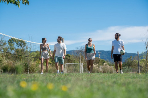 Cuatro adultos caminan cerca de una red de voleibol en el parque vacacional Sandaya Etruria en la Toscana, Italia.