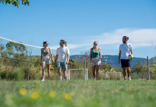 Fire voksne går på en græsplæne nær et volleyballnet på Sandaya Etruria feriepark i Toscana, Italien.