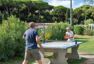 Deux personnes jouent au tennis de table en plein air au Sandaya Etruria, en Toscane, Italie, entourés de verdure.