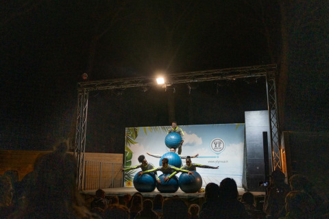 Artister optræder på scenen med blå bolde foran et publikum om aftenen i Sandaya Etruria, Toscana.