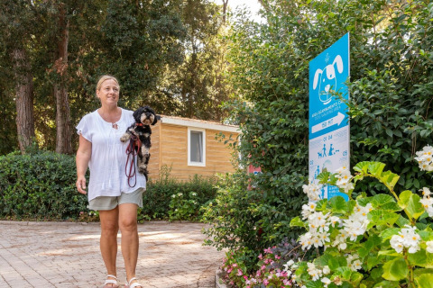 Donna che passeggia con un piccolo cane al Sandaya Etruria, villaggio vacanze in Toscana, Italia, vicino a un cartello per cani.