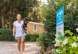 Mujer paseando con un perro pequeño en Sandaya Etruria, un parque vacacional en la Toscana, Italia, junto a un cartel para perros.
