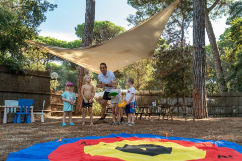 Des enfants et un adulte jouent dehors sous une toile d’ombrage au Sandaya Etruria en Toscane, Italie.