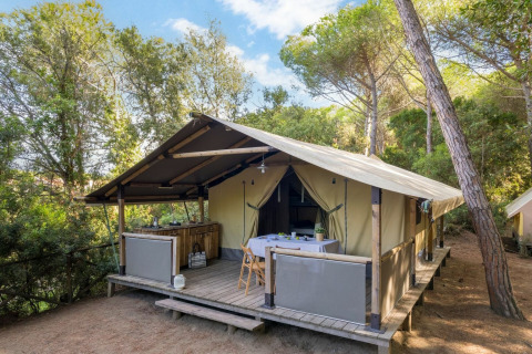Tienda safari Tent Kenya con porche de madera y mesa al aire libre, rodeada de bosque tranquilo.