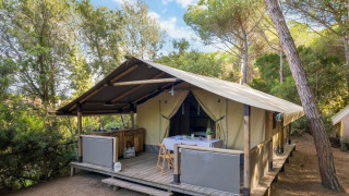 Tienda safari Tent Kenya con porche de madera y mesa al aire libre, rodeada de bosque tranquilo.