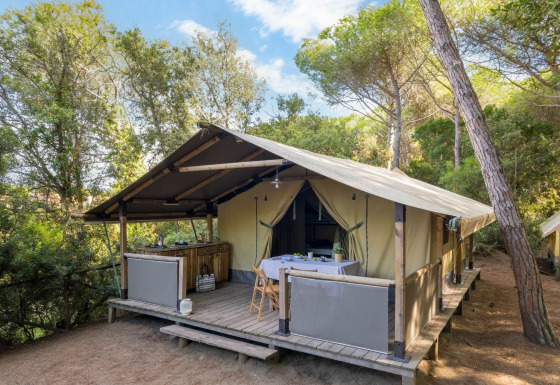 Tienda safari Tent Kenya con porche de madera y mesa al aire libre, rodeada de bosque tranquilo.
