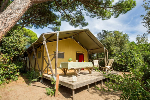 Lodge Safari tent met houten terras, tafel en stoelen, genesteld tussen bomen in de natuur.