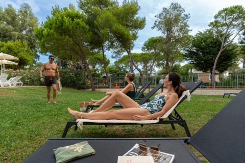 Gæster slapper af på liggestole ved Sandaya Toscana Bella feriepark i Toscana, Italien, omgivet af træer.