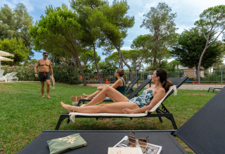 Guests relaxing on loungers at Sandaya Toscana Bella holiday park in Tuscany, Italy, surrounded by trees.