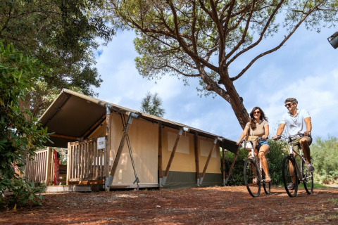 Een stel fietst langs een glampingtent op Sandaya Toscana Bella vakantiepark in Toscane, Italië.