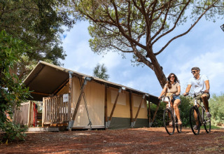 Een stel fietst langs een glampingtent op Sandaya Toscana Bella vakantiepark in Toscane, Italië.