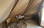 Interior de una tienda Tipi Junior en Weekend Glamping Resort, Italia, con mesa, sillas y alfombra.