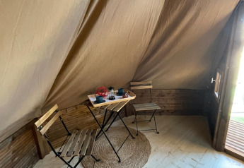Interior de una tienda Tipi Junior en Weekend Glamping Resort, Italia, con mesa, sillas y alfombra.