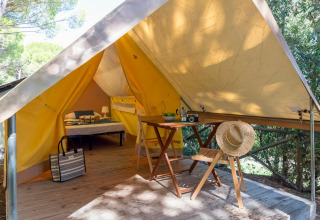Safari-Zelt Tent Aventure bei Sandaya Etruria in Italien mit Bett, Tisch, Stühlen und Strohhut auf Holzterrasse.