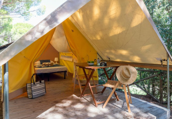 Safari tent at Sandaya Etruria in Italy, featuring a bed, table, chairs, and straw hat on a wooden terrace.