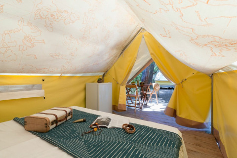 Inde i et safari-telt med stor seng, mini-køleskab og udendørs siddeområde hos Sandaya Etruria, Italien.