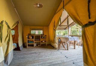 Interior de una tienda safari con suelo de madera y zona de comedor en Tent Kenya, Sandaya Etruria, Italia.