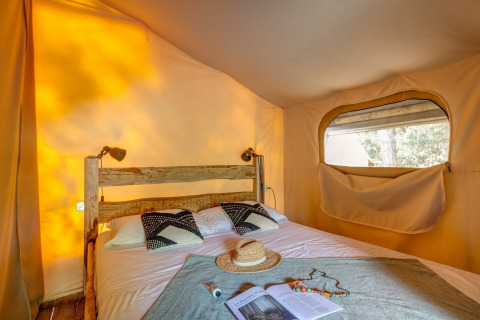 Innenaufnahme des Safari-Zelts Tent Kenya im Sandaya Etruria, Italien, mit rustikalem Bett und Sonnenlicht.
