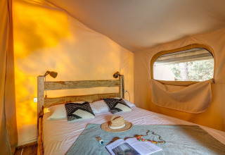 Innenaufnahme des Safari-Zelts Tent Kenya im Sandaya Etruria, Italien, mit rustikalem Bett und Sonnenlicht.