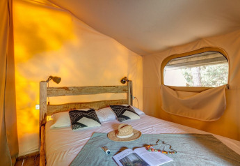 Vista interior de la tienda de safari Tent Kenya en Sandaya Etruria, Italia, con cama rústica y luz natural.