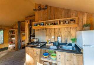 Keukengedeelte in een safaritent van Country Lodge bij Sandaya Etruria in Italië, met hout en kleurrijk servies.