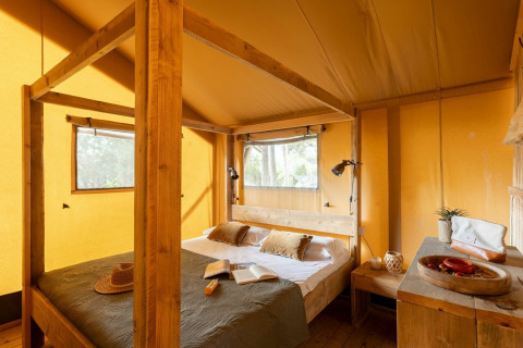 Gemütliches Schlafzimmer im Safarizelt der Country Lodge im Sandaya Etruria, Italien, mit Holzmöbeln.