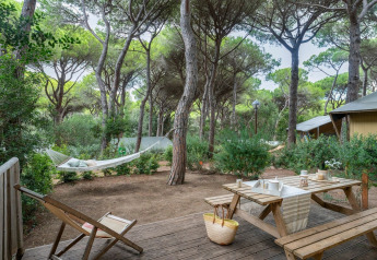 Wooden terrace at Country Lodge Large safari tent, Sandaya Etruria, Italy, with hammock and picnic bench in forest.