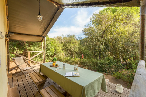 Overdekt terras met houten tafel en banken bij Lodge Safari in Sandaya Etruria, Italië, tussen de bomen.