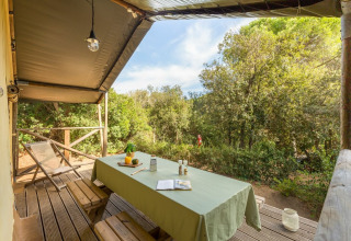Overdekt terras met houten tafel en banken bij Lodge Safari in Sandaya Etruria, Italië, tussen de bomen.