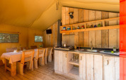 Tienda safari espaciosa con cocina de madera y comedor en Sandaya Etruria, Italia, ambiente cálido.