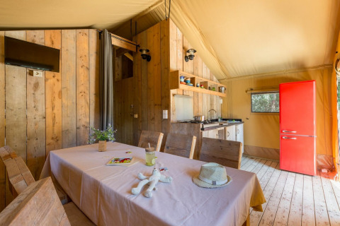 Interior de la tienda Lodge Safari en Sandaya Etruria, Italia, con mesa de comedor, cocina y nevera roja.