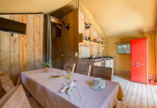 Interior de la tienda Lodge Safari en Sandaya Etruria, Italia, con mesa de comedor, cocina y nevera roja.