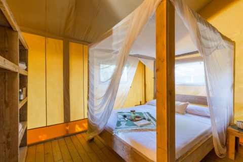 Binnenzicht van de Lodge Safari-tent bij Sandaya Etruria in Italië met hemelbed en warme sfeerverlichting.