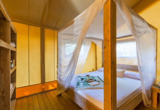 Binnenzicht van de Lodge Safari-tent bij Sandaya Etruria in Italië met hemelbed en warme sfeerverlichting.