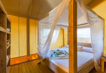 Interior de la tienda Lodge Safari en Sandaya Etruria, Italia, con cama con dosel y luz cálida natural.